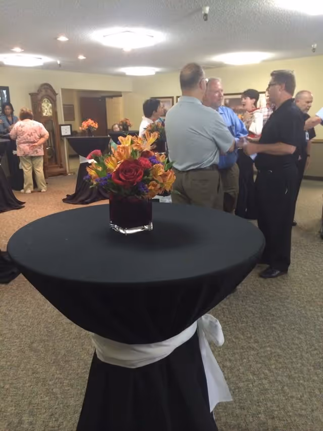 Communal event room with people mingling around high-top tables topped with floral centerpieces.