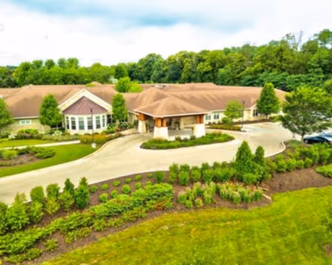 Aerial view of a single-story senior living building with a covered circular driveway, manicured landscaping, and trees in the background.