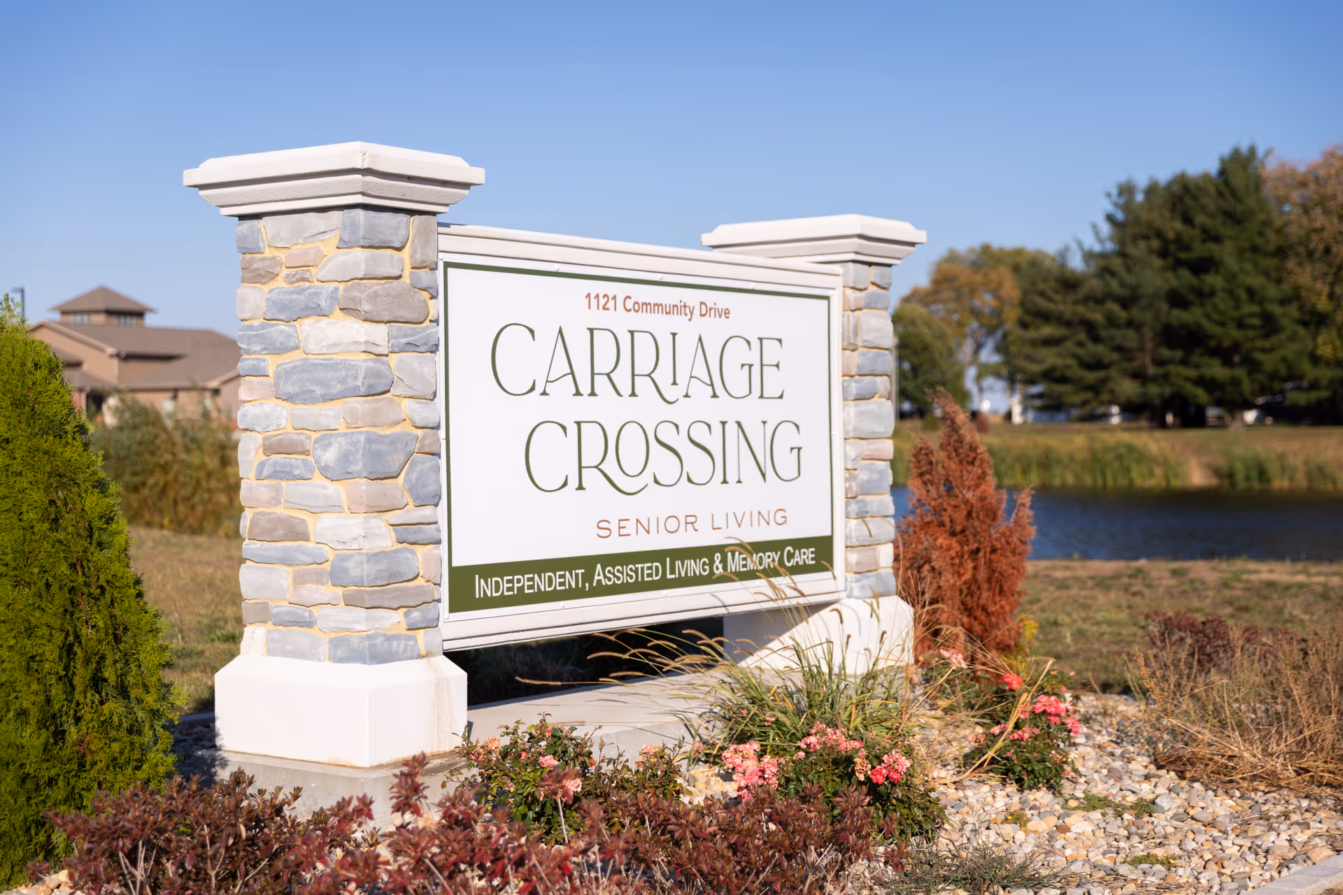 Stone entrance sign reading "Carriage Crossing Senior Living" by a pond and landscaped grounds.