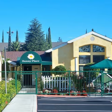 Sunny Place of Stockton building exterior with yellow walls, green gate, and patio seating.