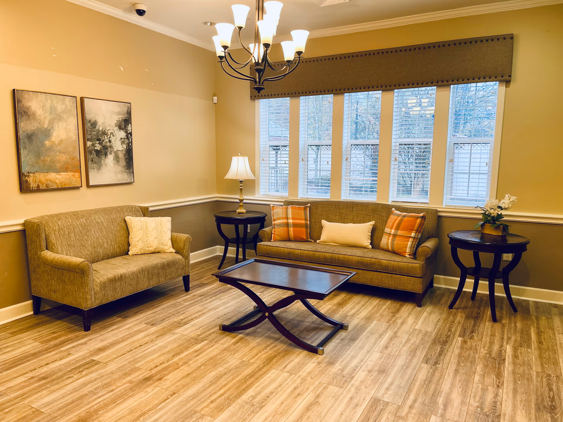 Cozy living room with two sofas, a coffee table, side tables and lamp, a row of windows, and a chandelier.