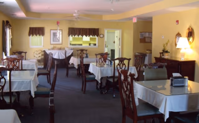 Dining room with multiple tables covered in white tablecloths and wooden chairs in a softly lit interior.