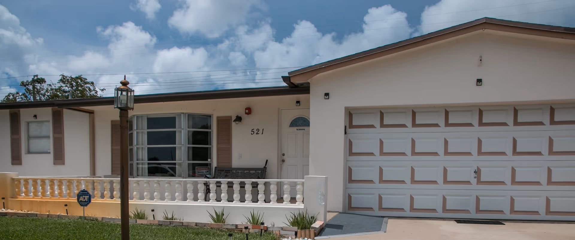 Front exterior of a single-story building with a porch, balustrade, lamp post, and a two-car garage labeled 521.