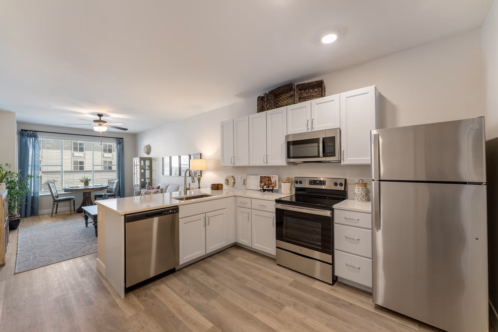 Bright modern open kitchen with white cabinets, stainless steel appliances, and an island overlooking a living/dining area.