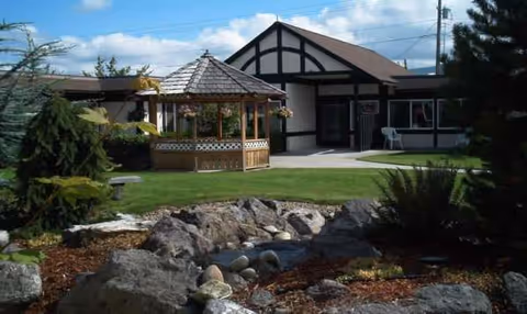 Exterior view of Sherwood Assisted Living with a gazebo, rocks, and manicured lawn.