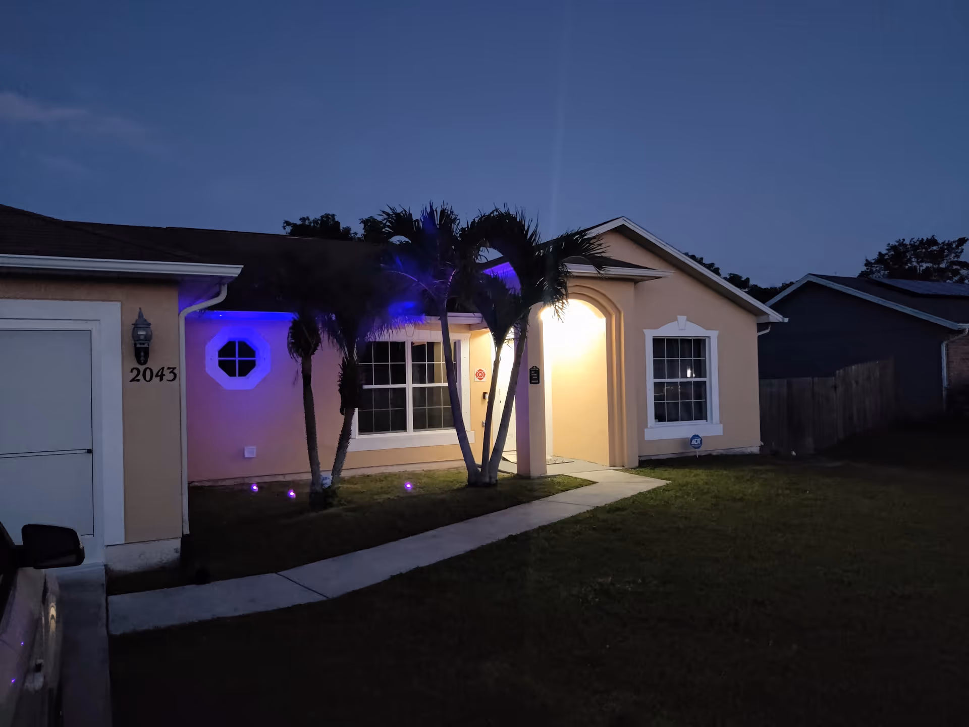 Front exterior of a single-story house at dusk with an illuminated entryway, palm trees, and the house number 2043.