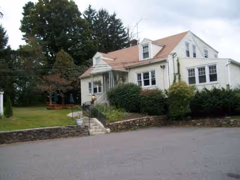 White, suburban-style senior living building front with steps and manicured shrubs.