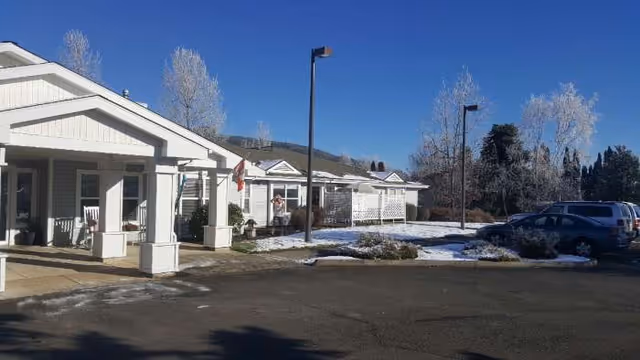 Exterior view of Applegate Place senior living facility with white porches, parked cars, and light snow.