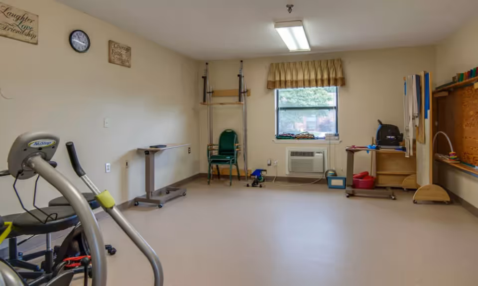 Small interior therapy/activity room with exercise equipment, chairs, a window and wall-mounted therapy bars.
