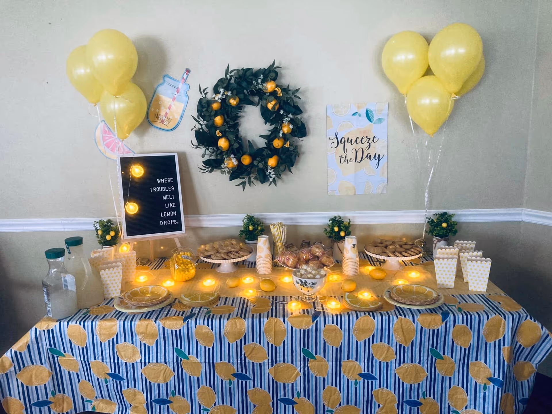 Indoor dining area display with lemon-themed party table, balloons, wreath, and lights.