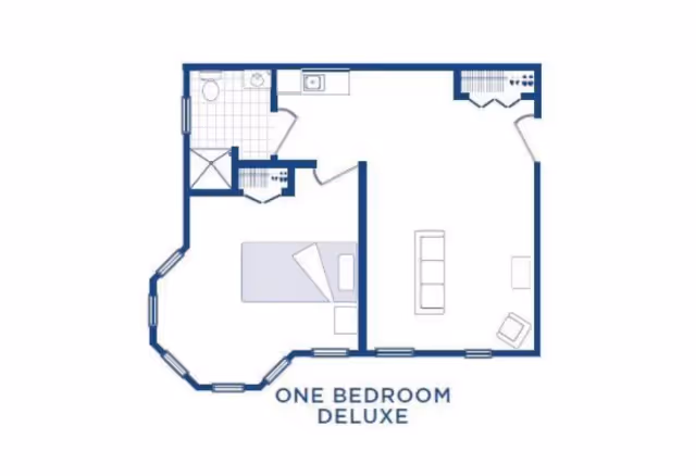 Floor plan layout of a one bedroom deluxe apartment showing a bedroom with a bed, a bathroom with a shower and sink, a kitchen area, and a living room with a sofa and chair.