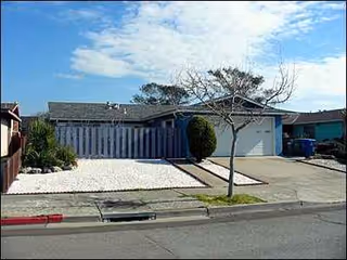 Front exterior of a single-story blue building with driveway, tree, and white gravel landscaping.