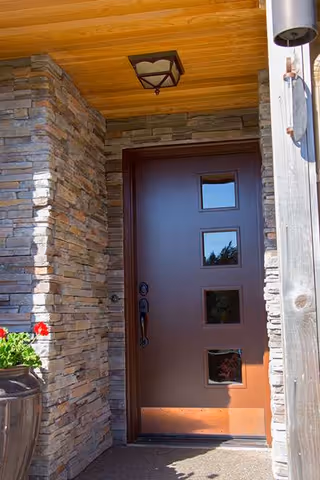 Front entrance of Canyon Creek AFH with stone walls, brown door with square windows and planter