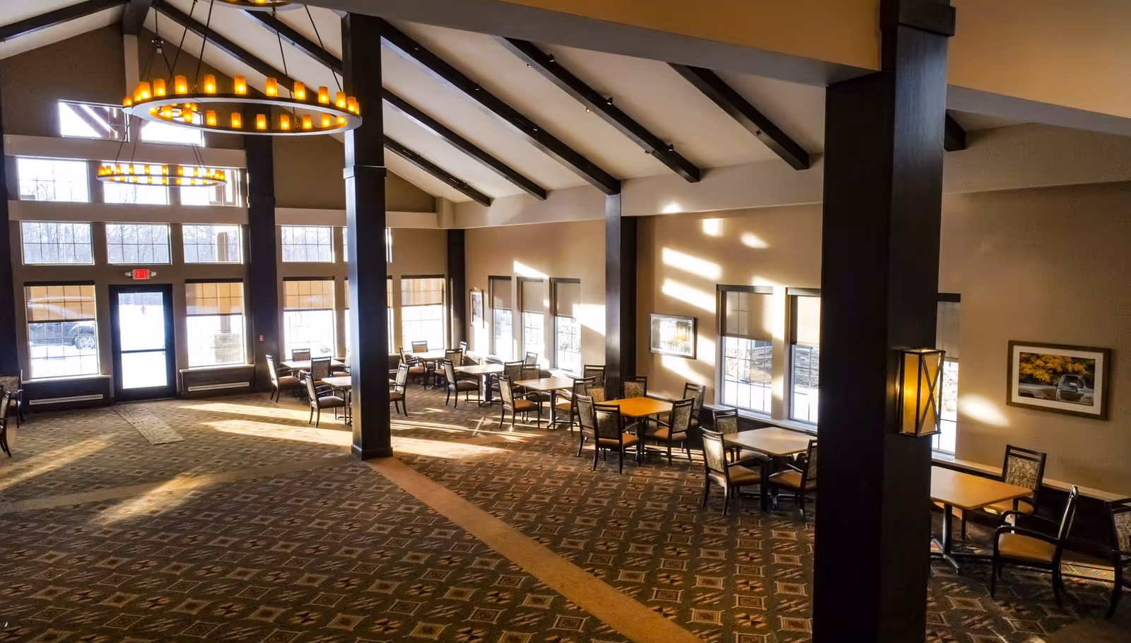 Bright, spacious dining/common room with multiple tables and chairs, high beamed ceiling, and large windows.