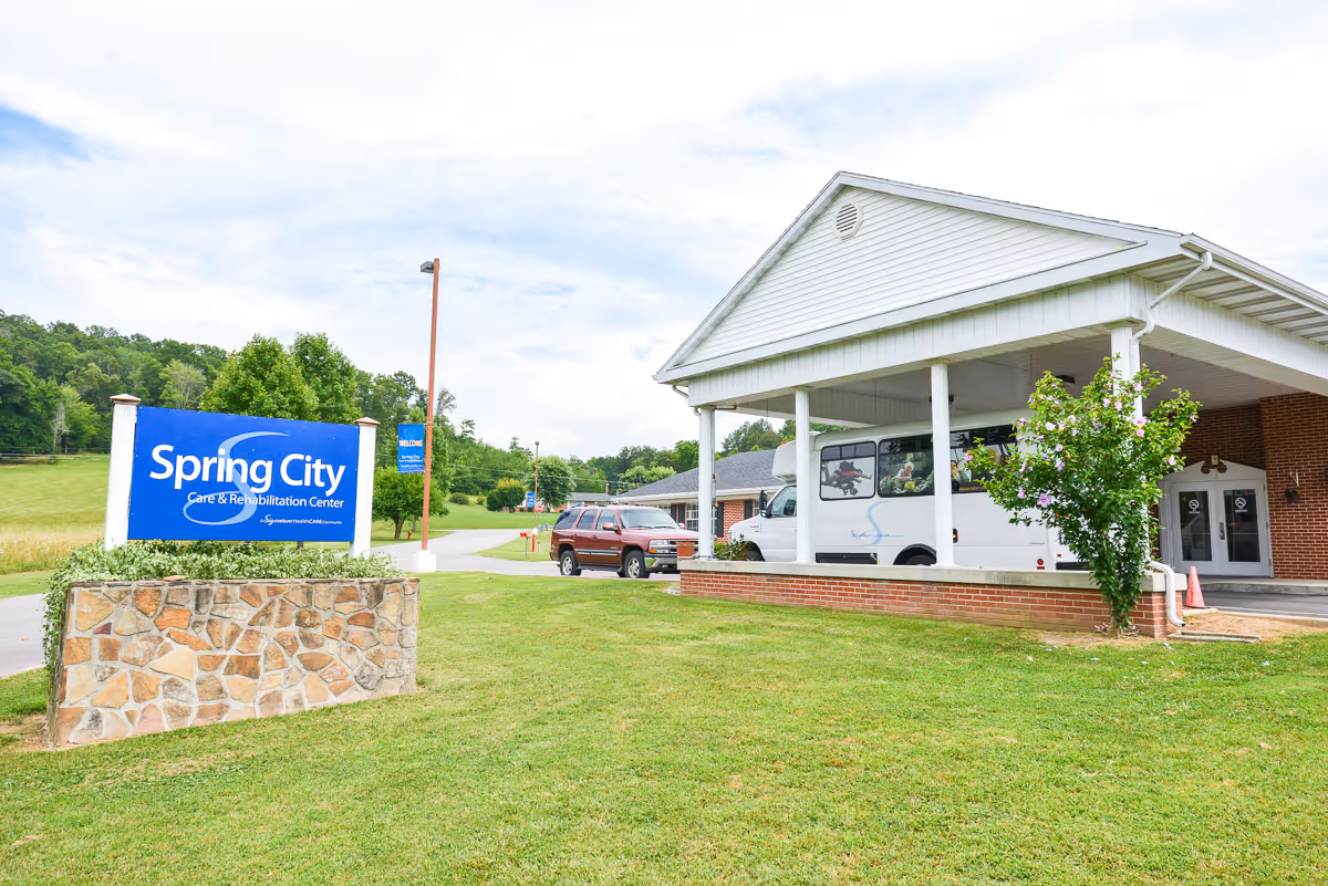 Exterior view of Spring City Care and Rehabilitation Center showing the front entrance, a blue sign, and a white bus.