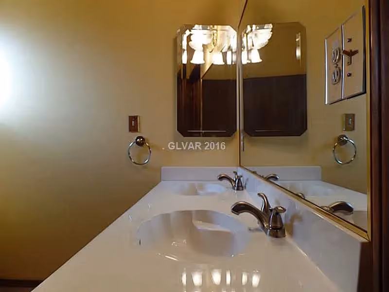 Bathroom vanity with dual sinks, chrome faucets, and a large mirrored wall reflecting a light fixture.