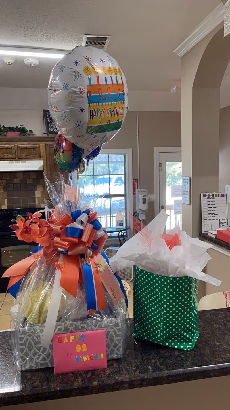 Gift baskets with balloons and a 'Happy Birthday' card on a counter in a communal kitchen area.