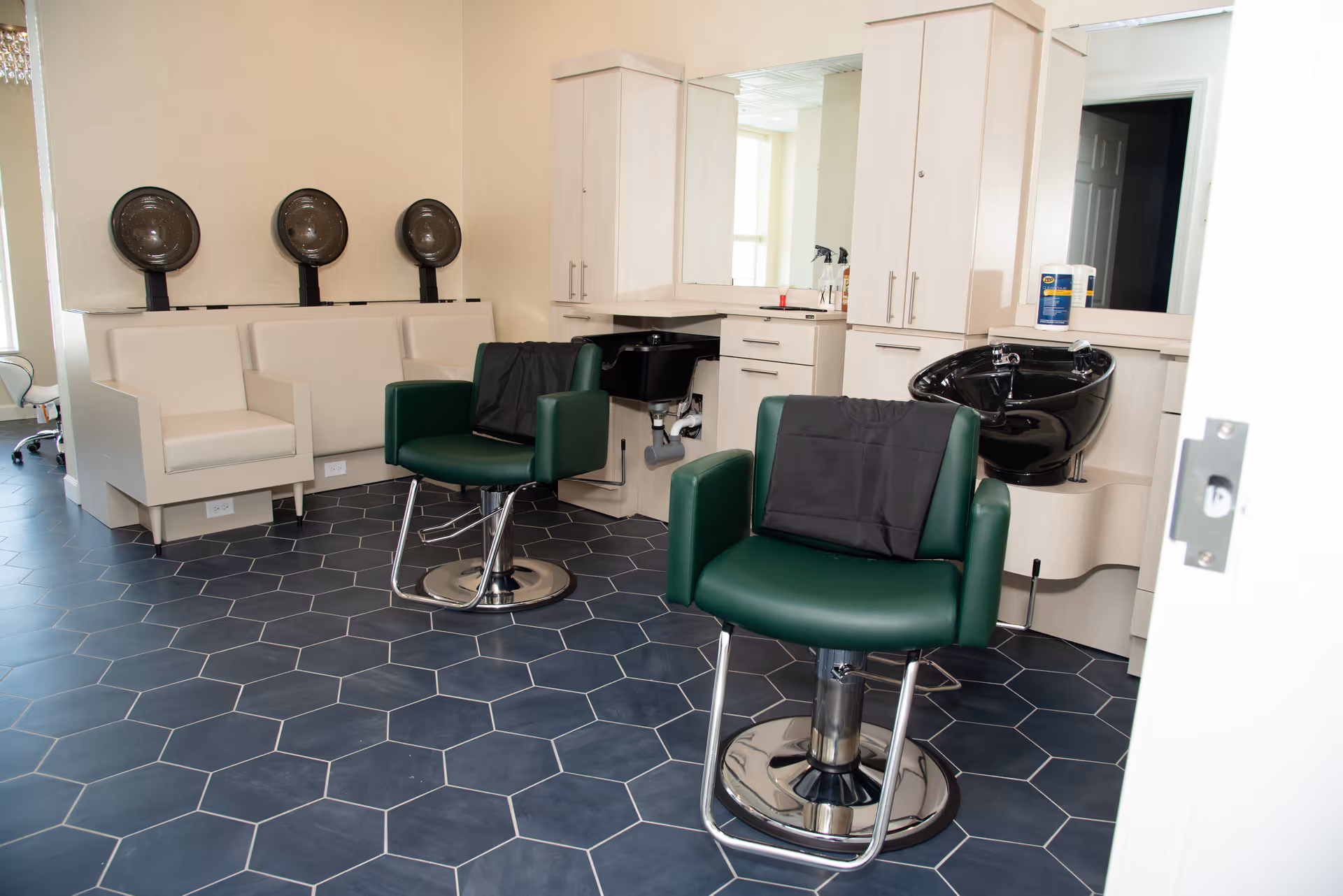 Interior salon with green styling chairs, hair-wash sinks, and hooded dryers.