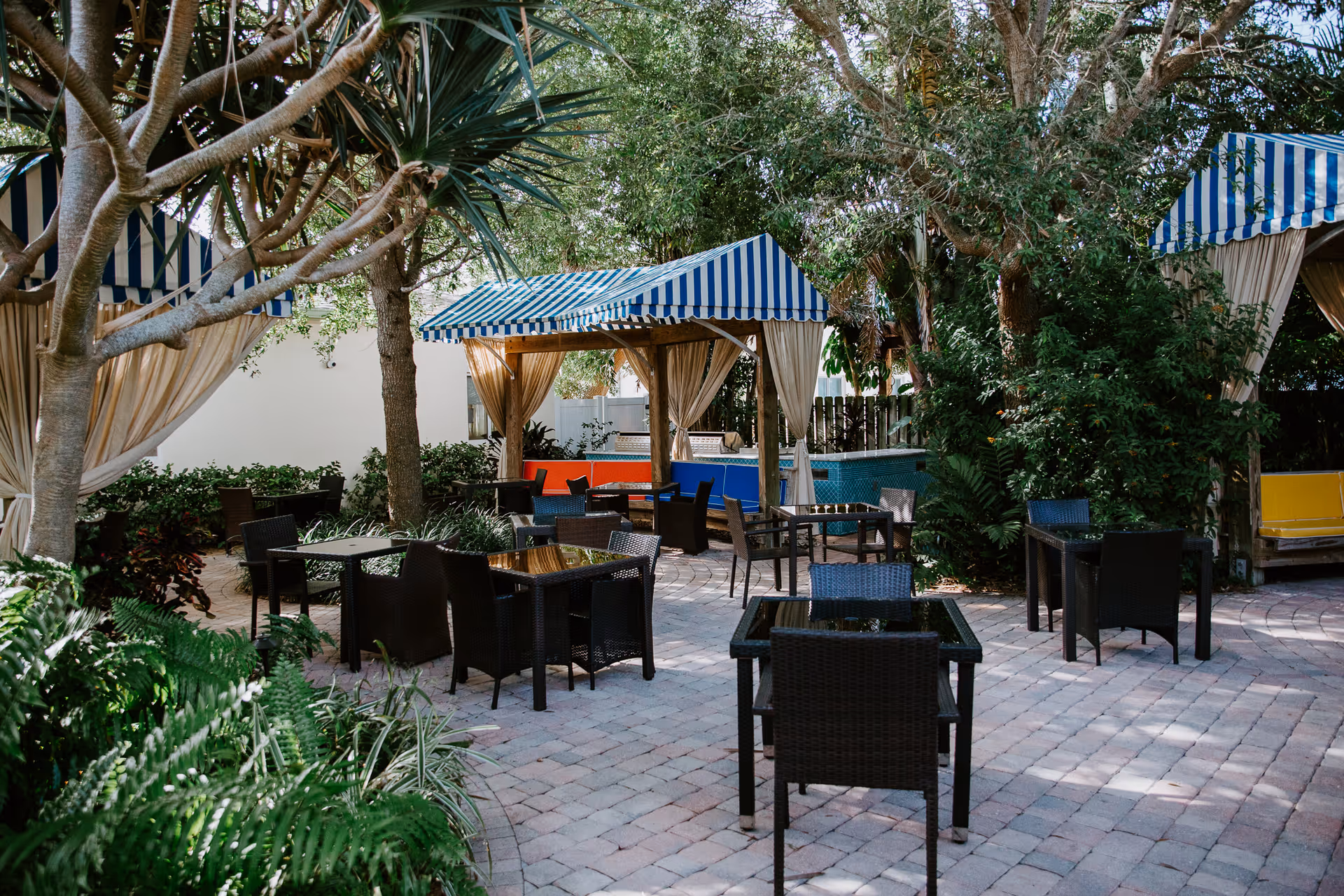 Outdoor patio with striped canopies, wicker tables and chairs among lush trees.