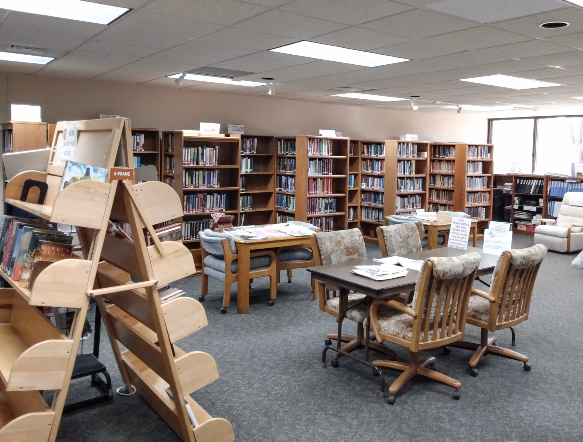 Community library room with bookshelves, tables and chairs in a senior living facility.