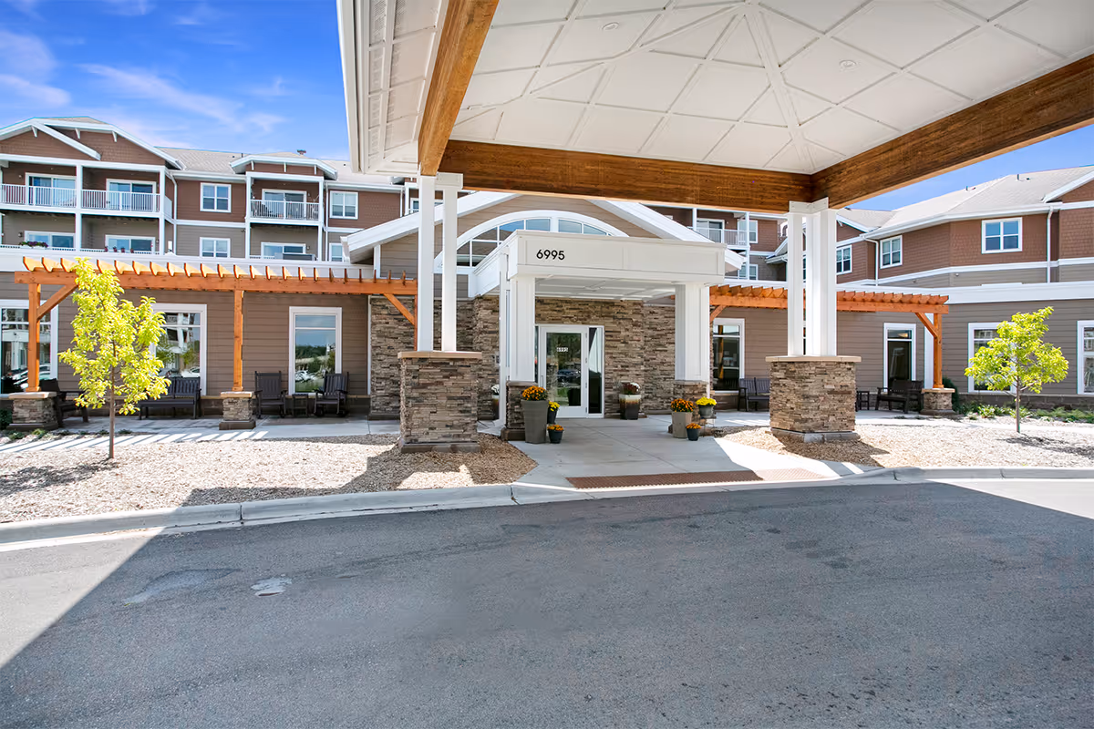 Front entrance of a multi-story senior living building with a covered porte-cochere, stone columns, and balconies.