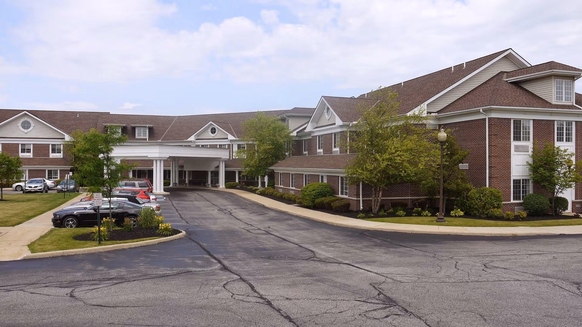 Front exterior of Parkside Villa, a two-story brick senior living building with a covered entrance, driveway and parked cars.