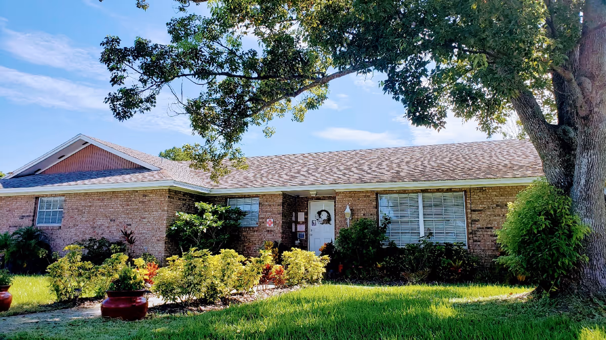 Single-story brick building with a landscaped front yard, large tree, and a central entry door.