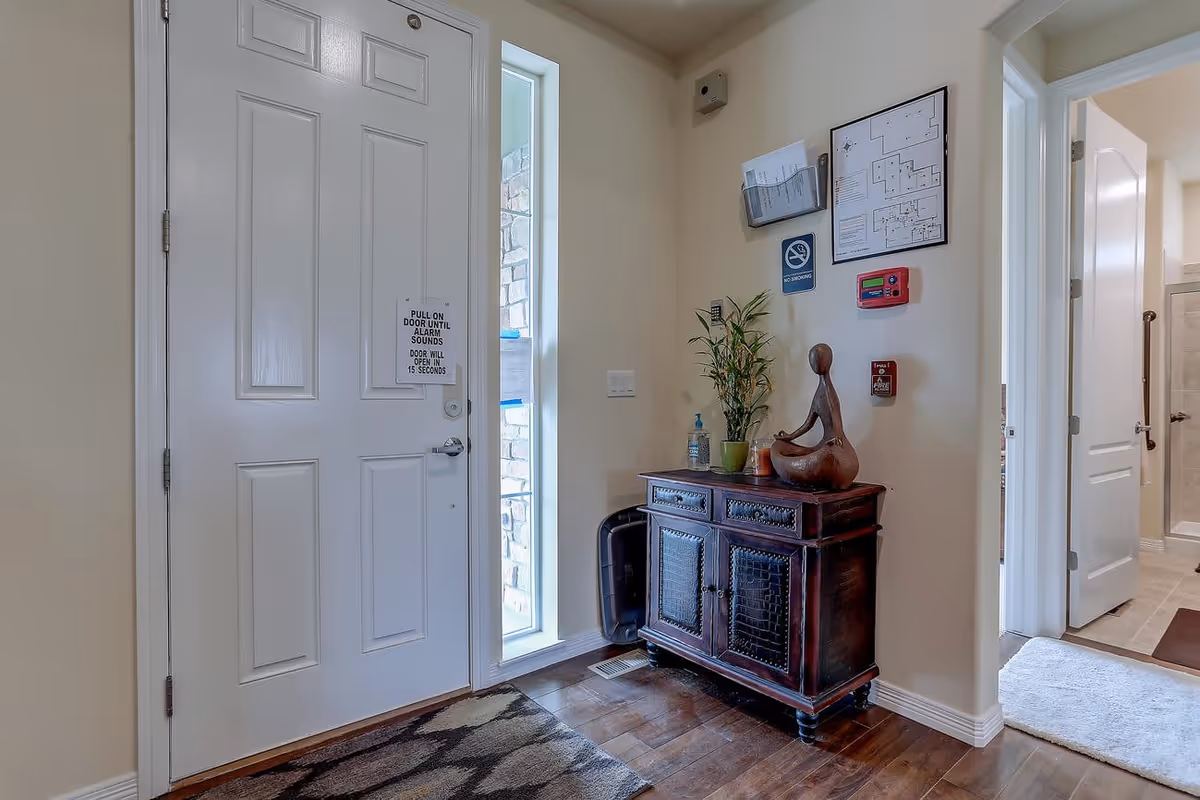 Entryway interior showing a closed white front door with a narrow sidelight, a wooden console table topped with a plant and sculpture, and a hallway to adjoining rooms.