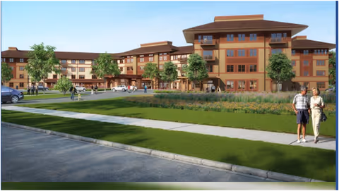 Exterior view of a large multi-story senior living facility with landscaped green lawns, trees, and a sidewalk. Two people are walking on the sidewalk in the foreground.