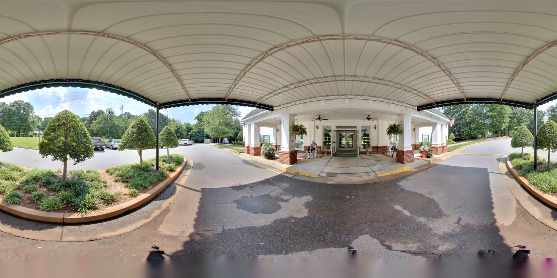 Covered porte-cochere entrance to Oaks at Tucker with brick columns, hanging plants, landscaped islands and a driveway.