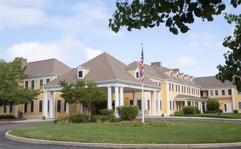 Exterior view of Coachman Square at Woodbridge, a yellow building with columns and flag.