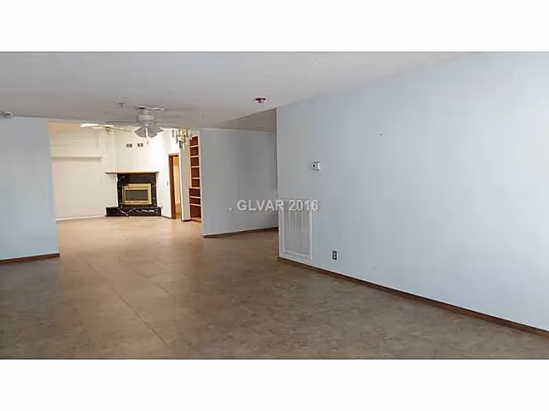 Empty open living room with tiled floor, ceiling fan, and a fireplace in the background.