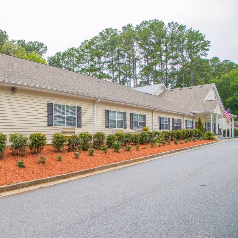 Long, single-story beige senior living building with shutters and neatly landscaped front.
