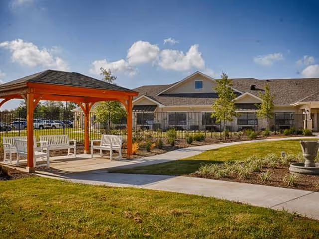 Exterior view of a senior living campus with an orange gazebo and white benches.