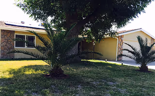 Front exterior of a single-story senior living facility with stone columns and palm trees.