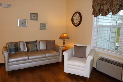 Cozy living room at The Meadows at Sun Valley with sofa, armchair, lamp, clock, blinds.