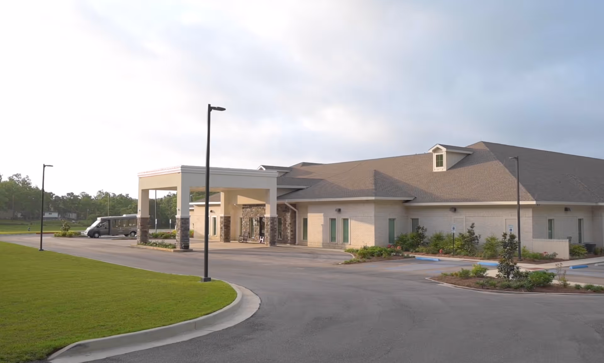 Front exterior of a single-story building with a covered drop-off entrance, parking lot, and landscaped lawn.