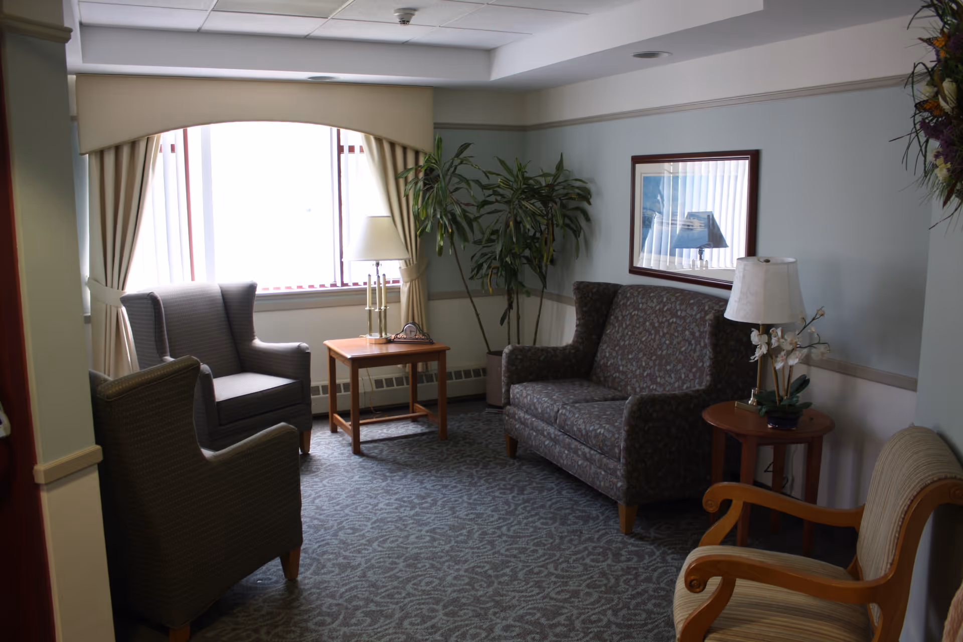 A cozy sitting area with armchairs, a loveseat, side tables, lamps, framed art and a window with curtains.