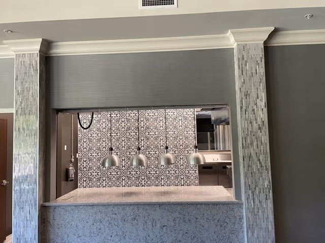 Serving counter pass-through with four hanging metal pendant lights and a patterned tile backsplash opening into a kitchen.