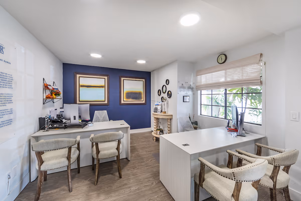 Bright reception area with two white desks, upholstered chairs, computer monitors, and framed artwork on a navy accent wall.