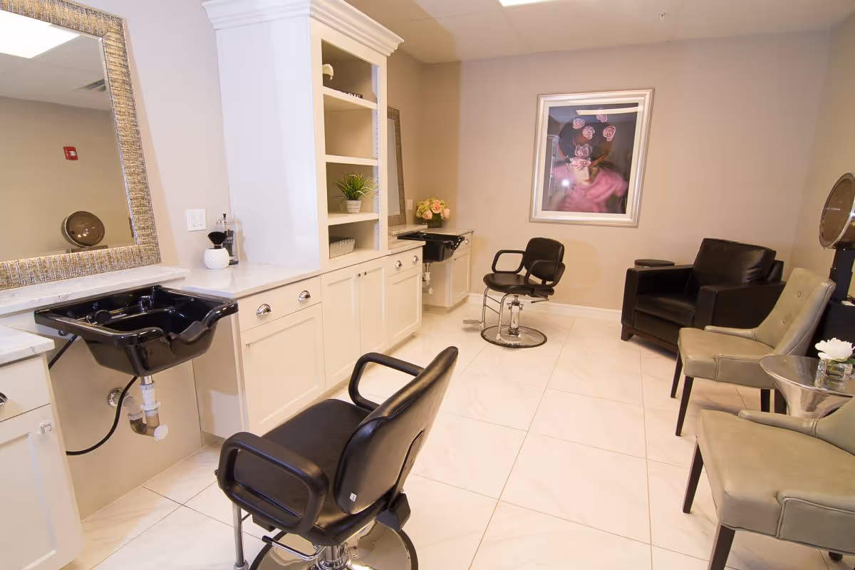 Salon-style room with styling chairs, black hair-washing sinks, cabinets and a small seating area.