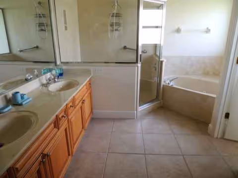 Double-sink vanity, wooden cabinets, mirrors, and a glass shower with a bathtub in the bathroom.