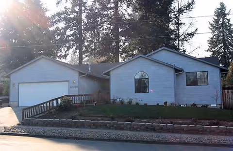 A single-story blue building with a two-car garage and landscaped front yard.