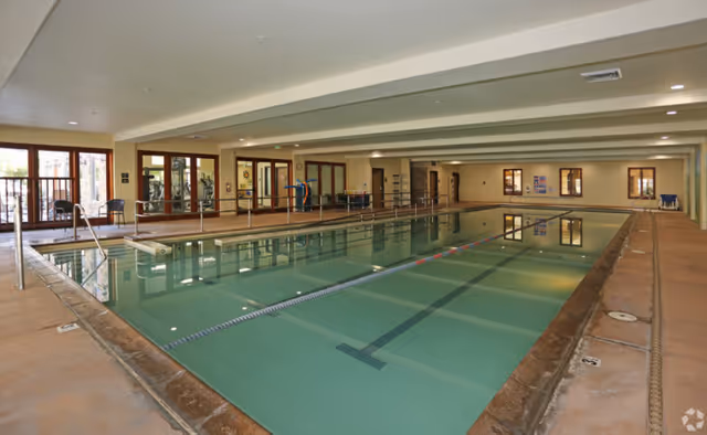 Indoor community swimming pool with lap lanes, handrails, and seating along the sides.