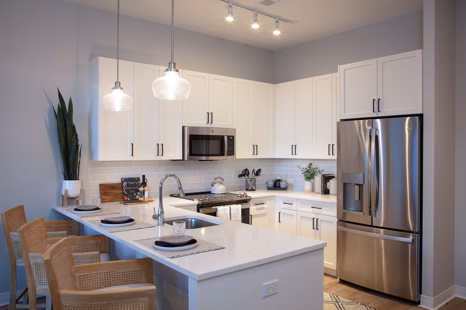 Bright modern kitchen with white cabinets, a large island with seating, stainless steel refrigerator and microwave, and pendant lights.
