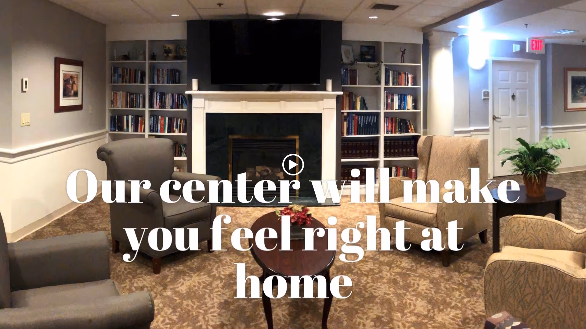 Cozy common room with armchairs arranged around a coffee table facing a fireplace and built-in bookshelves.
