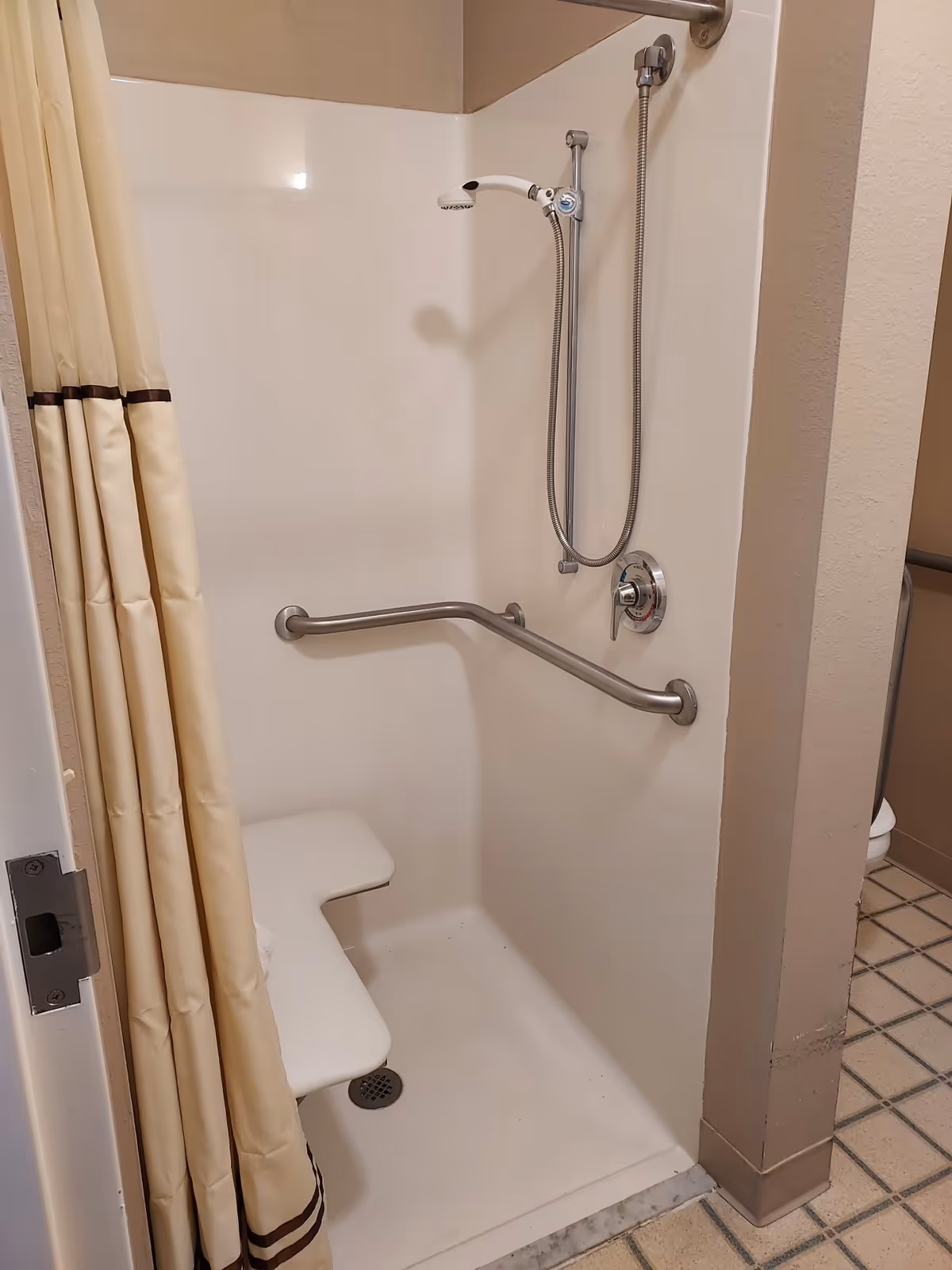 Accessible shower stall with a fold-down seat, grab bars, handheld showerhead and a shower curtain.