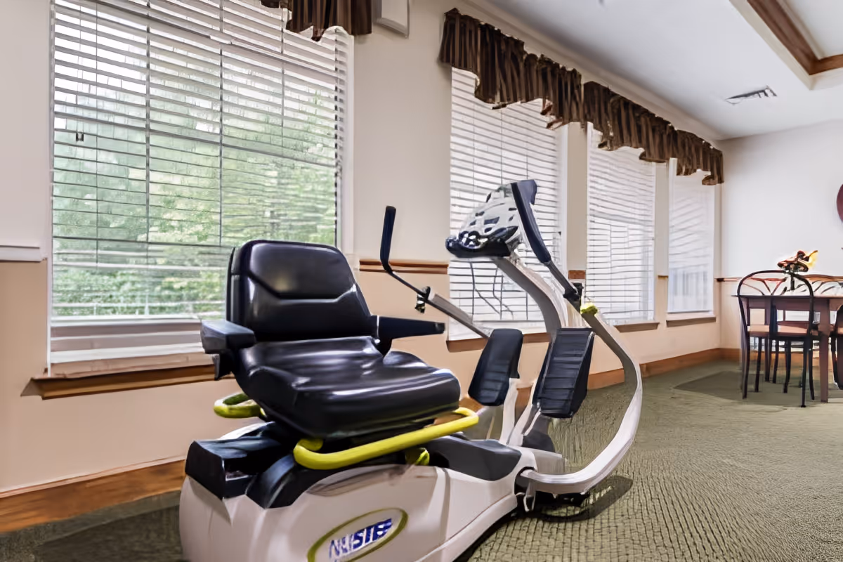 Interior room with a recumbent exercise machine by large windows and a small dining table in the background.