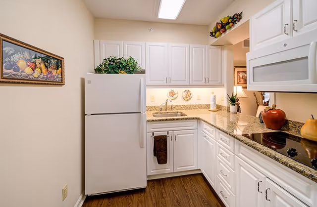 Small modern kitchen with white cabinets, a refrigerator, granite countertops, a sink, and an electric cooktop.