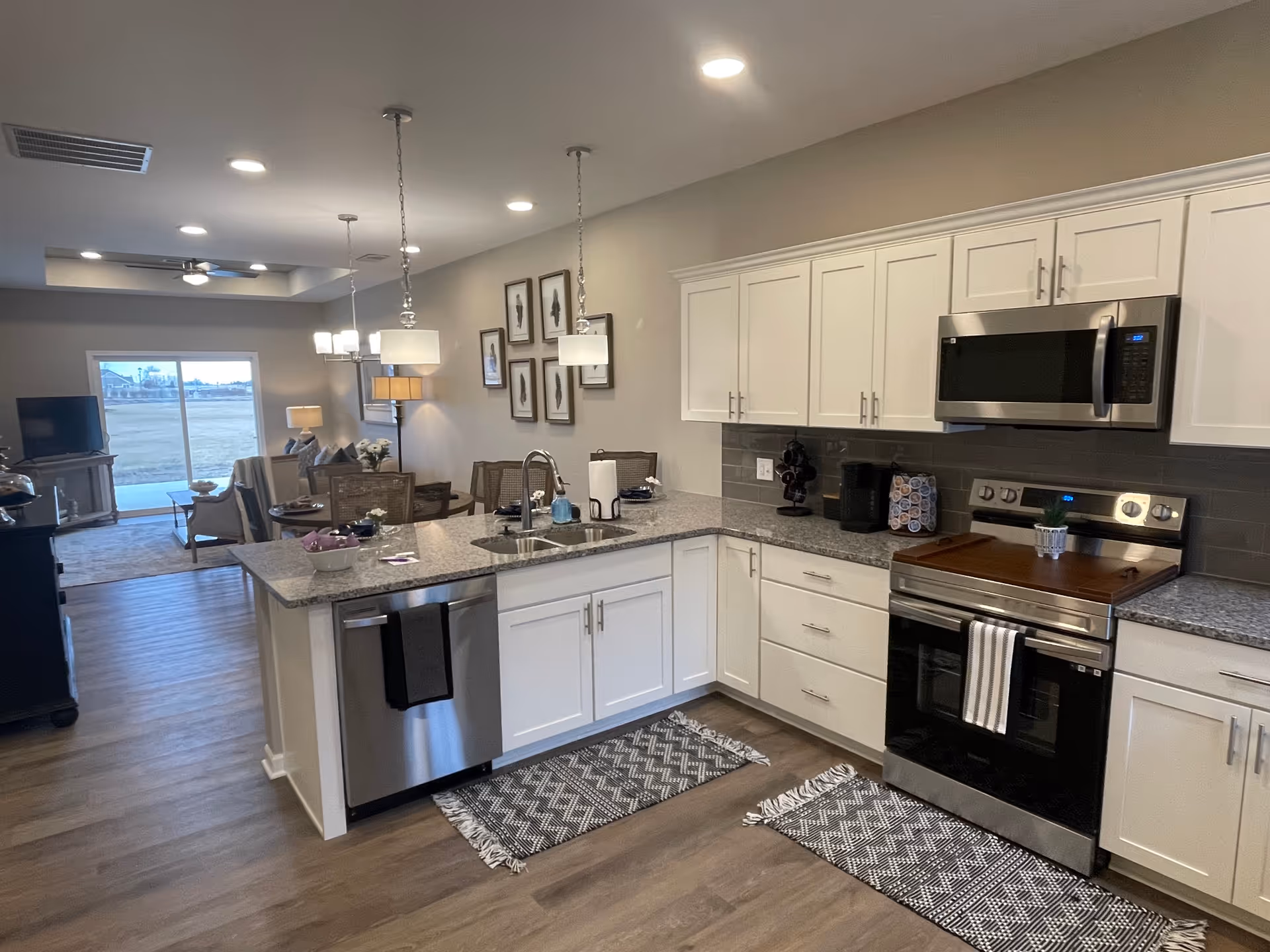 Open modern kitchen with white cabinets, stainless steel appliances, a granite-topped island and adjoining living/dining area.
